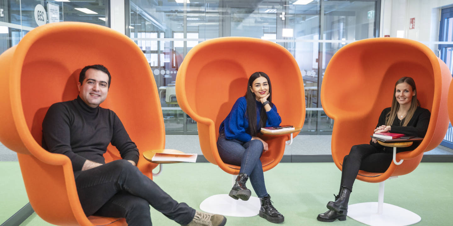 Three students sitting in big orange chairs smiling