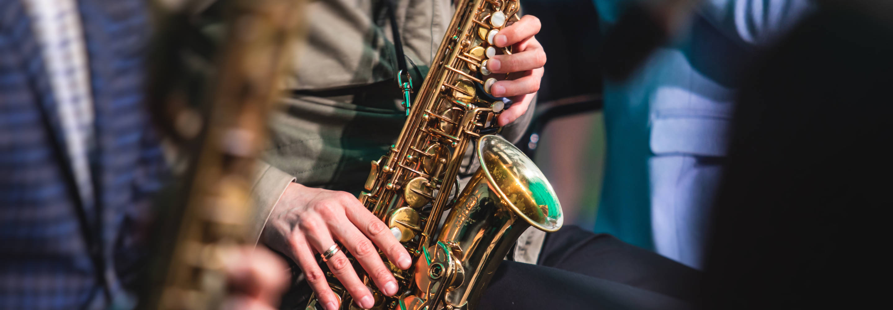 Kuvassa näkyy saksofoninsoittaja lähietäisyydeltä. Kuva rajautuu soittimen kohdalta niin, että soittajasta näkyvät vain kädet.