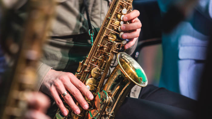 Kuvassa näkyy saksofoninsoittaja lähietäisyydeltä. Kuva rajautuu soittimen kohdalta niin, että soittajasta näkyvät vain kädet.