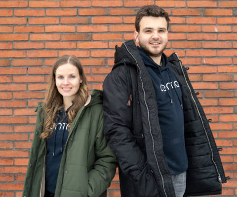 Two centrians, a woman and a man wearing the Centria hoodie while standing in front of a brick wall.