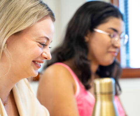 Two female students studying together at a table and laughing