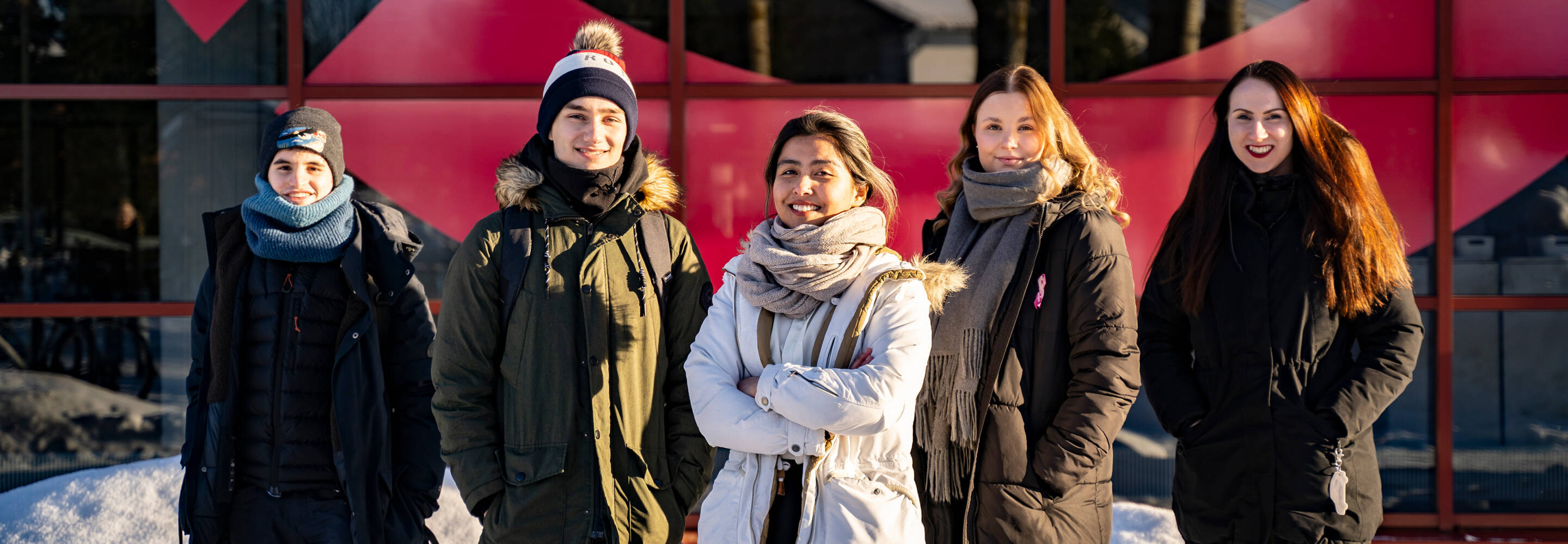 Five students photographed in front of the Talonpojankatu campus in winter, they pose for the camera and smile
