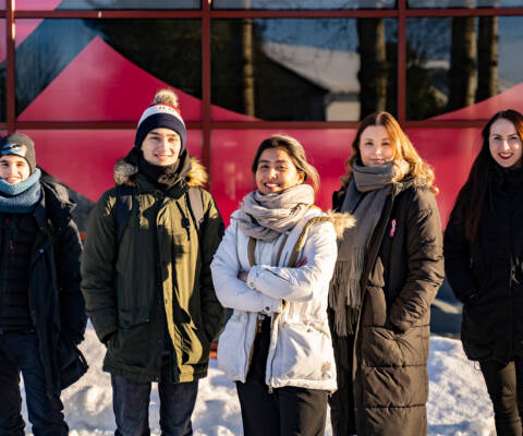 Viisi opiskelijaa poseeraa kameralle hymyillen Talonpojankadun kampuksen edustalla