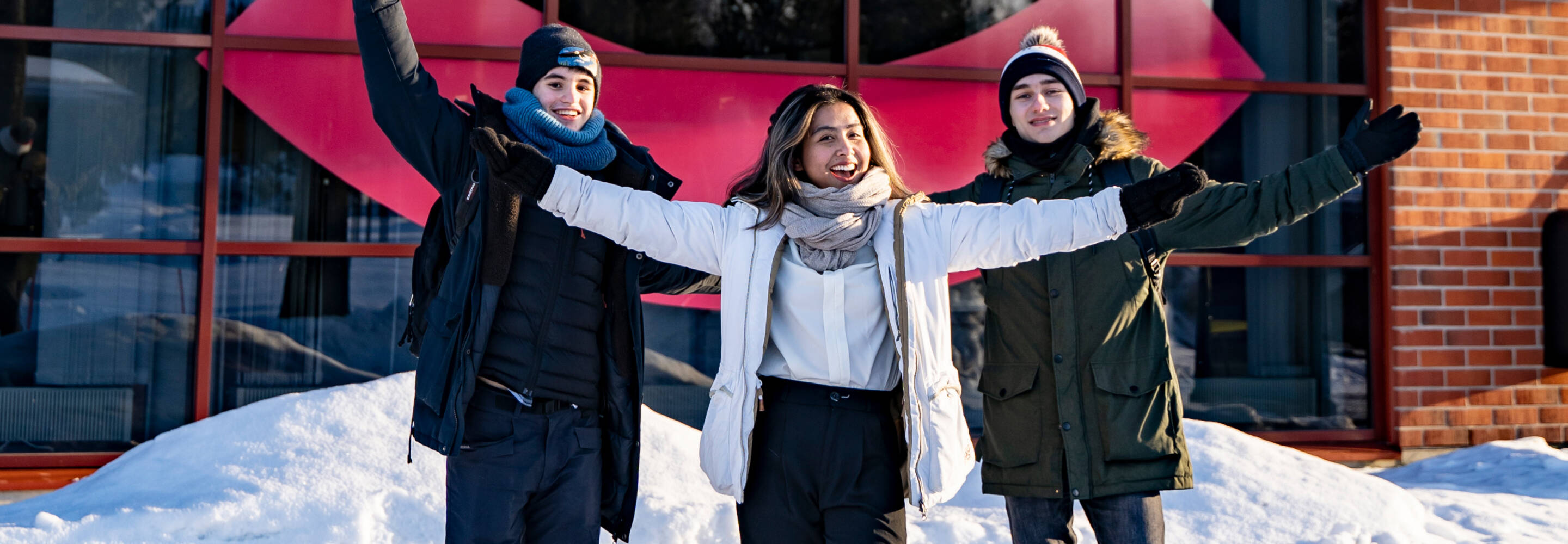 Three international students photographed in front of the Talonpojankatu campus in winter