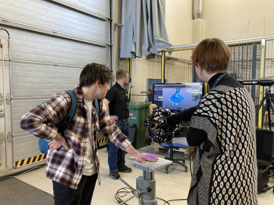Kolme henkilöä seisomassa ja testaamassa 3D-skannauslaitetta laboratorioympäristössä.