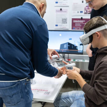 Asiantuntijat opastavat opiskelijaa VR-lasien käytössä. Taustalla näyttö, jossa näkyy virtuaalinen työmaasovellus.