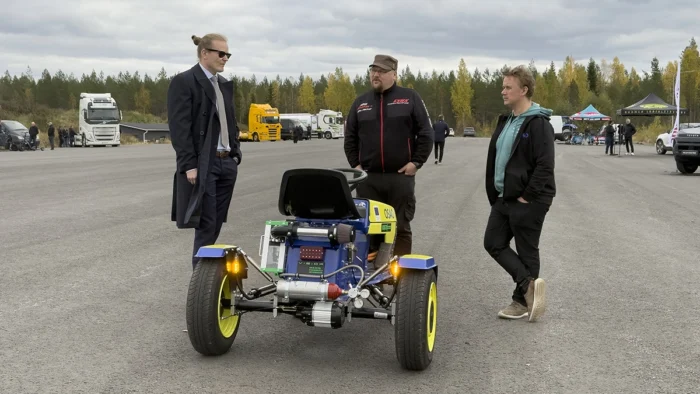 Kolme miestä keskustelemassa vakavasti pienen ajettavaa ruohonleikkuria muistuttavan vetyajoneuvon äärellä.
